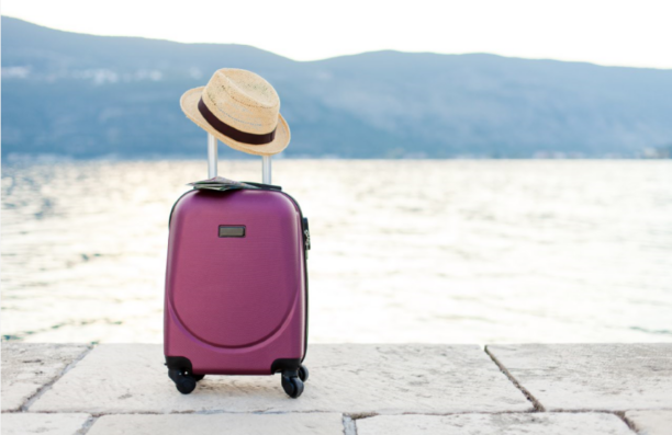 A pink suitcase with a straw hat and a map, with a view of the sea in the background